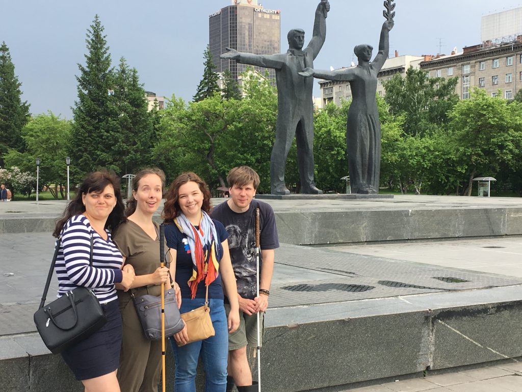 Laurel and Amy in the Novosibirsk city square with Aleksey and Olga. They are standing in front of two statues with arms outstretched.